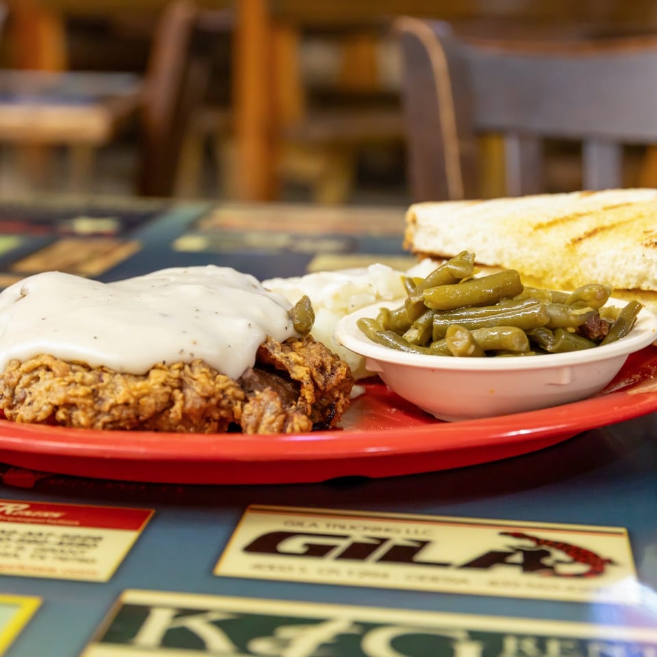 Chicken fried steak with cream gravy, green beans, mashed potatoes, and toast.