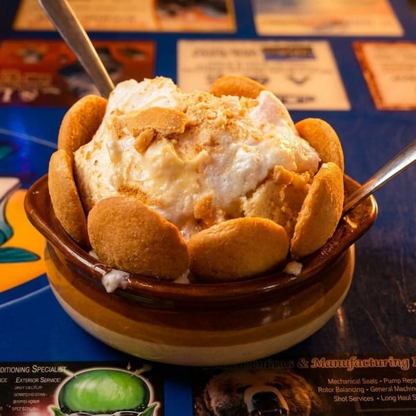 Banana pudding with vanilla wafers and whipped cream in a brown bowl on a blue placemat.
