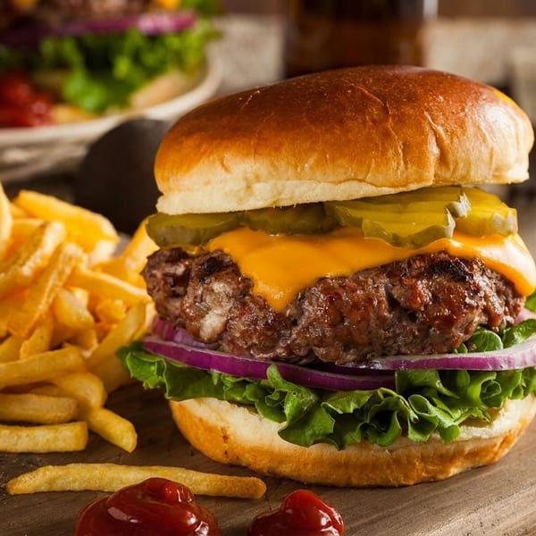 Cheeseburger with fries, ketchup, and a glass of beer on a wooden board.