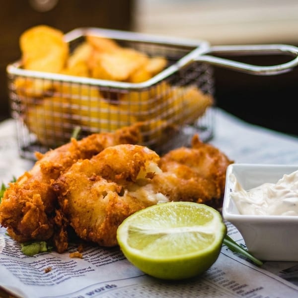 Crispy fried fish and chips served in a metal basket with a lime and tartar sauce.