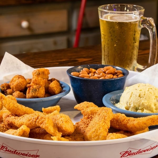 Fried fish, hush puppies, beans, and potato salad on a Budweiser tray with a beer.