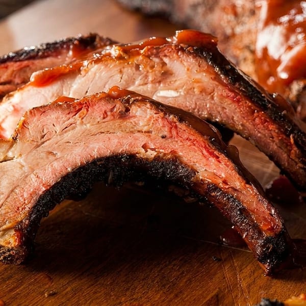 Close-up of juicy, saucy BBQ ribs with a smoke ring, resting on a wooden cutting board.